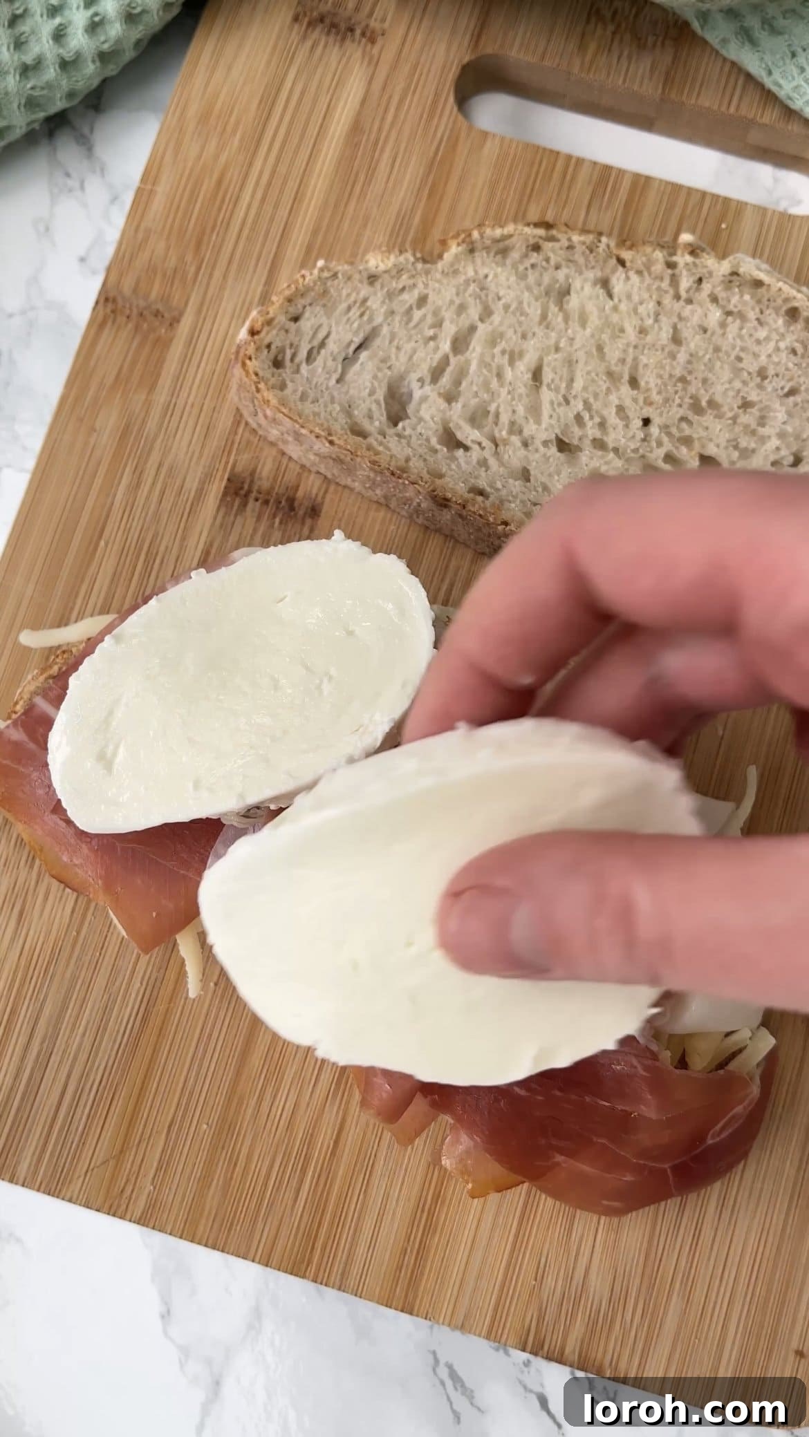 Laying grated cheese, prosciutto, and fresh mozzarella on a slice of sourdough bread