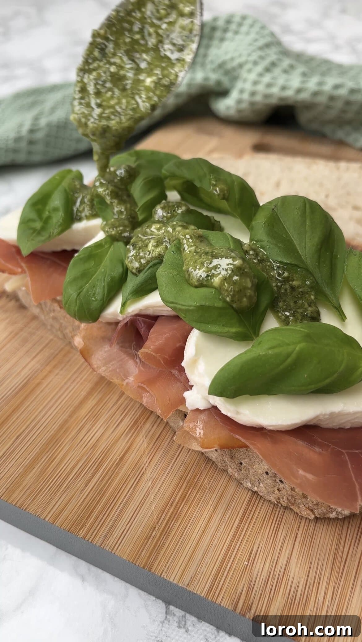Drizzling the sandwich fillings with fresh basil pesto and adding basil leaves