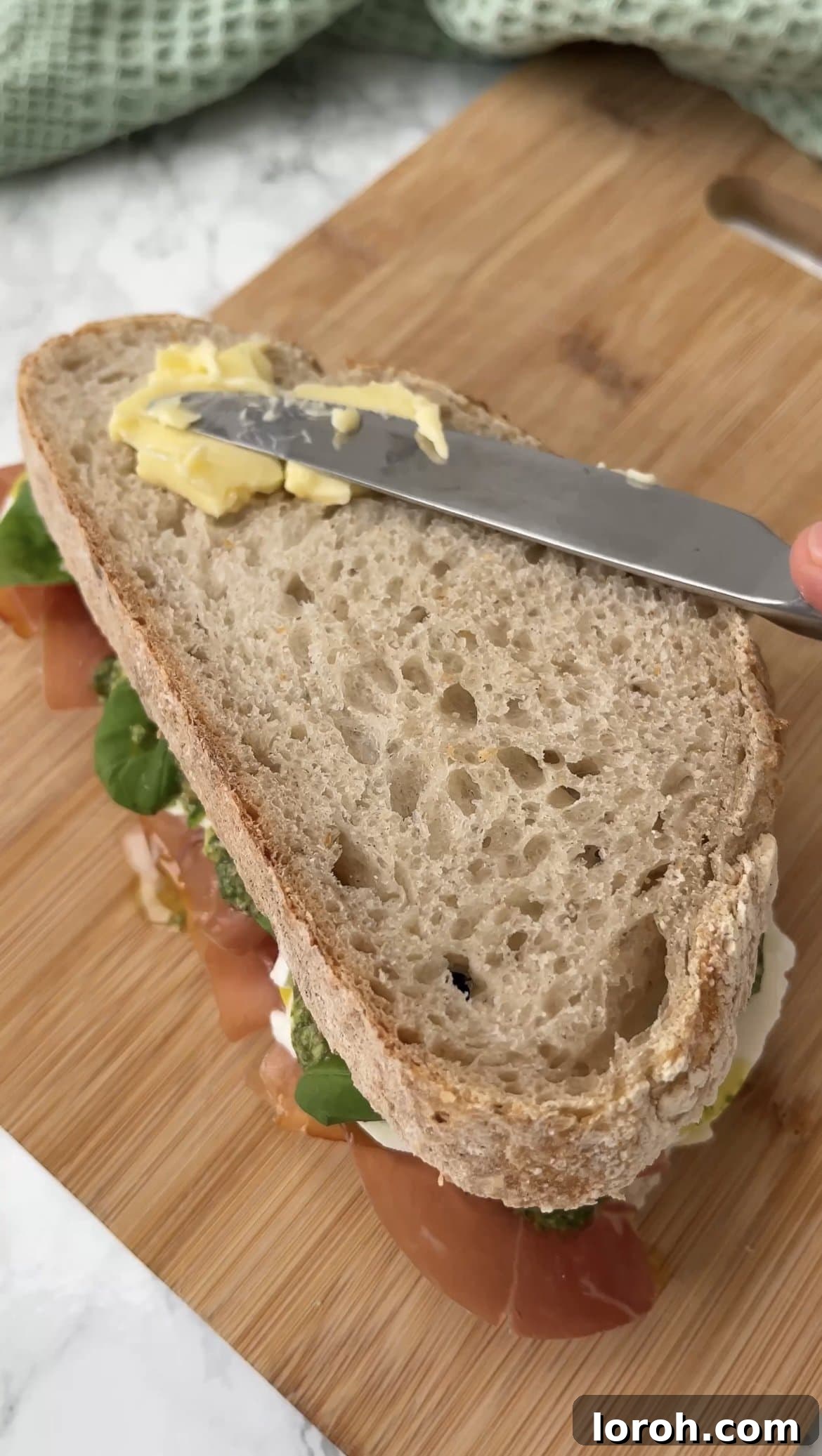 Generously buttering the exterior of the assembled sandwich for a golden crust