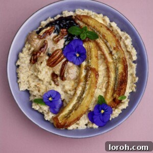 Creamy banana porridge topped with golden caramelised bananas, crunchy pecans, rich almond butter, and a dollop of vibrant blackberry jam, ready to be served in a rustic bowl.