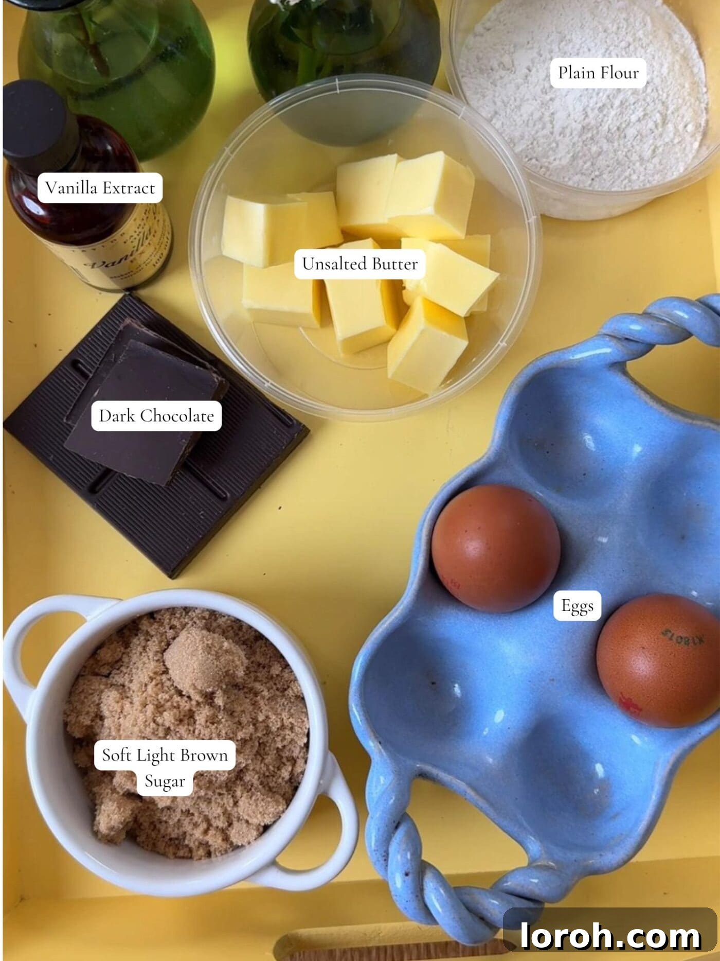 Molten Lava Chocolate Pudding 4 Key ingredients for melt-in-the-middle chocolate puddings arranged on a rustic surface, including chocolate, butter, sugar, and flour.