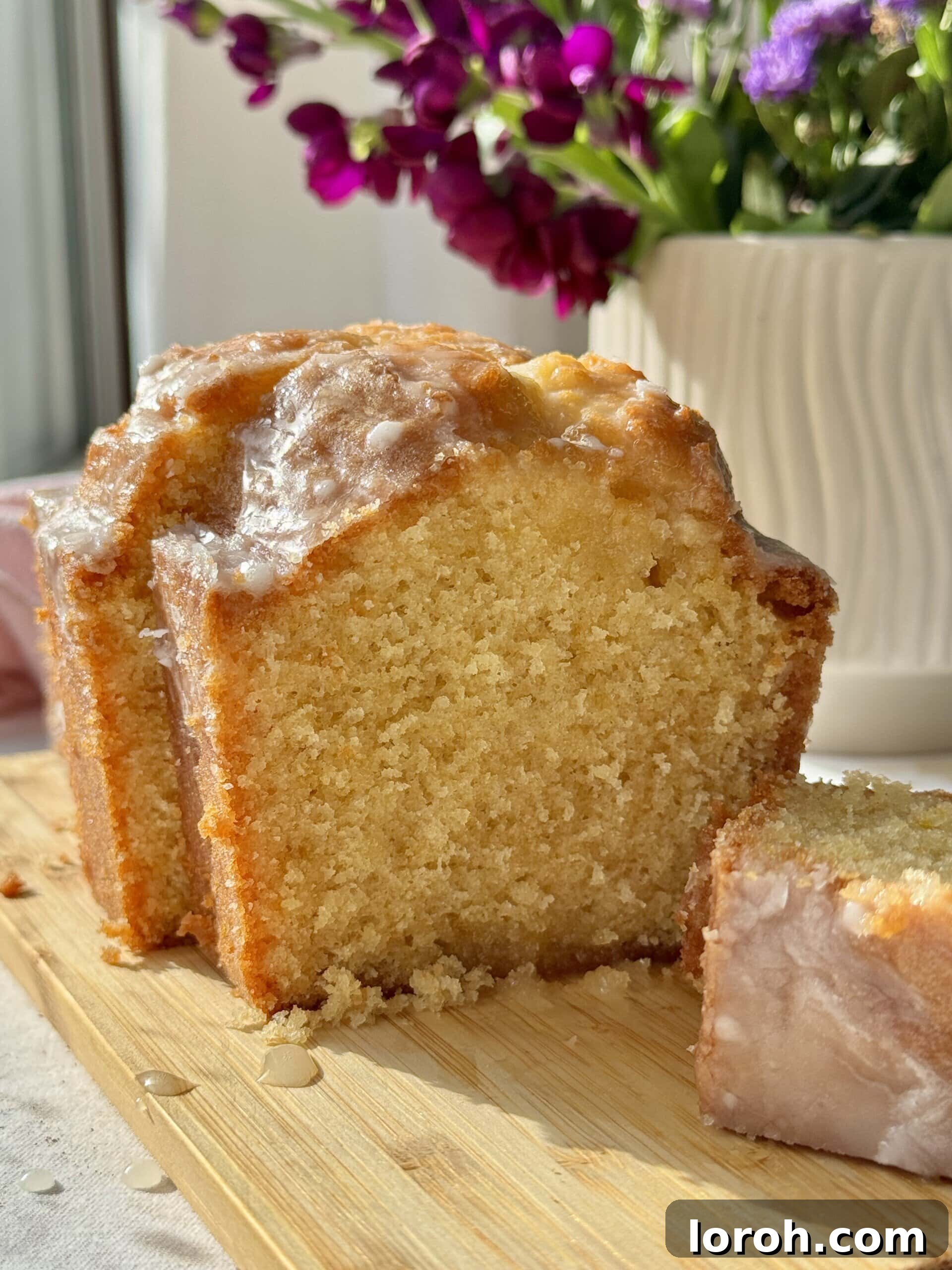 Sunshine Lemon Loaf 2 A perfectly sliced lemon loaf cake, revealing its moist texture and glistening lemon drizzle, presented on a rustic wooden board.