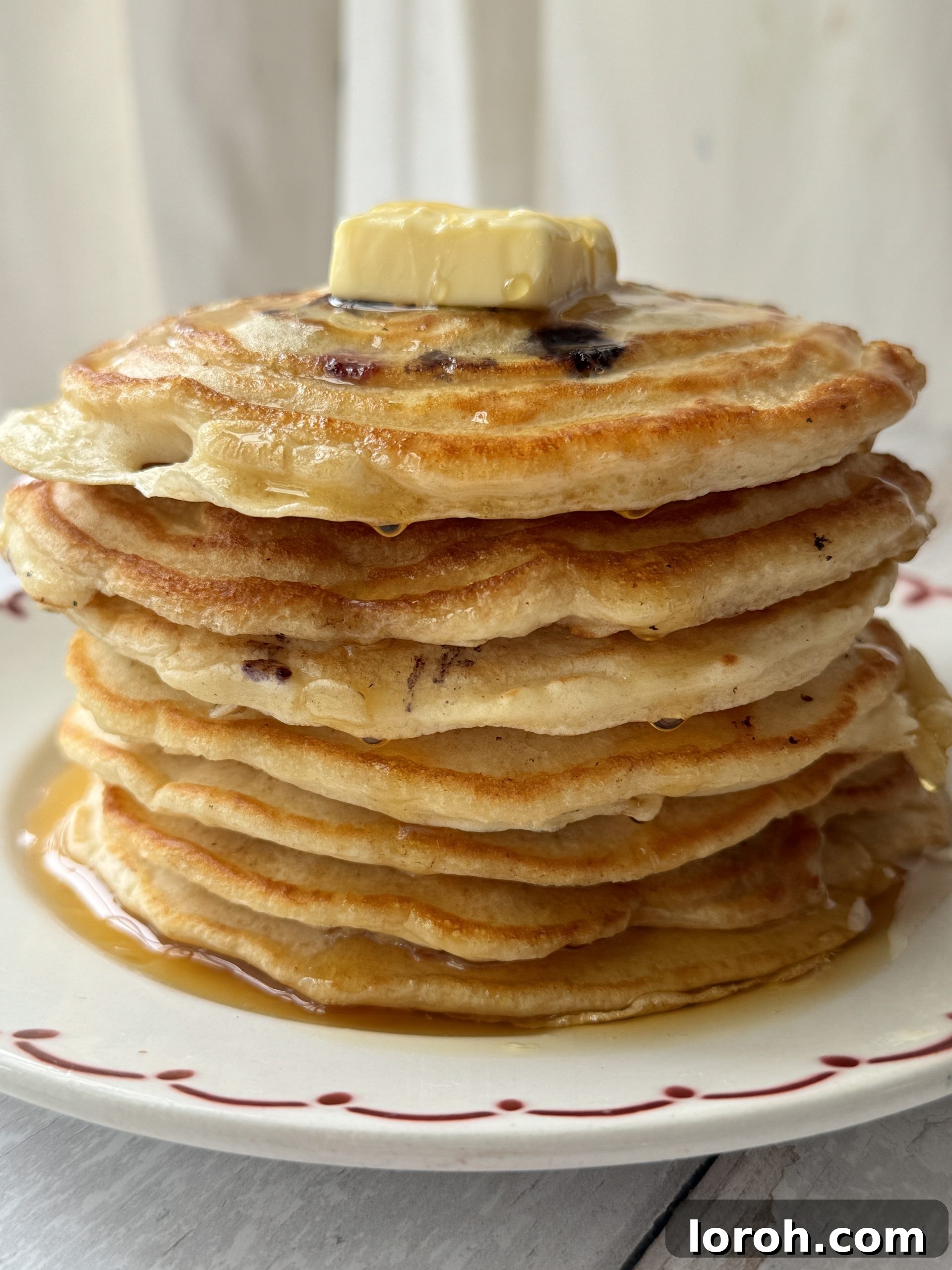 Effortless Fluffy Pancakes Without Baking Powder 2 A tall stack of golden pancakes, made without baking powder, drizzled with syrup and topped with fresh berries, on a white plate.
