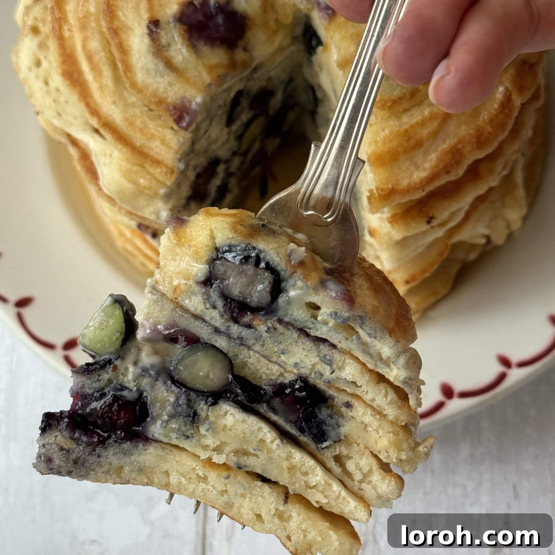 Effortless Fluffy Pancakes Without Baking Powder 8 A fork lifts a bite-sized piece of pancake, topped with fresh blueberries and syrup, showing its fluffy texture.