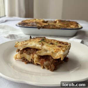 A slice of lasagne on a plate with the rest of the lasagne in the background, showcasing its delicious layers and golden top