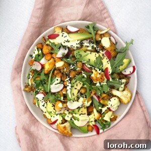 A vibrant bowl of roasted cauliflower and chickpea salad with fresh rocket, radishes, avocado slices, and a creamy green avocado dressing
