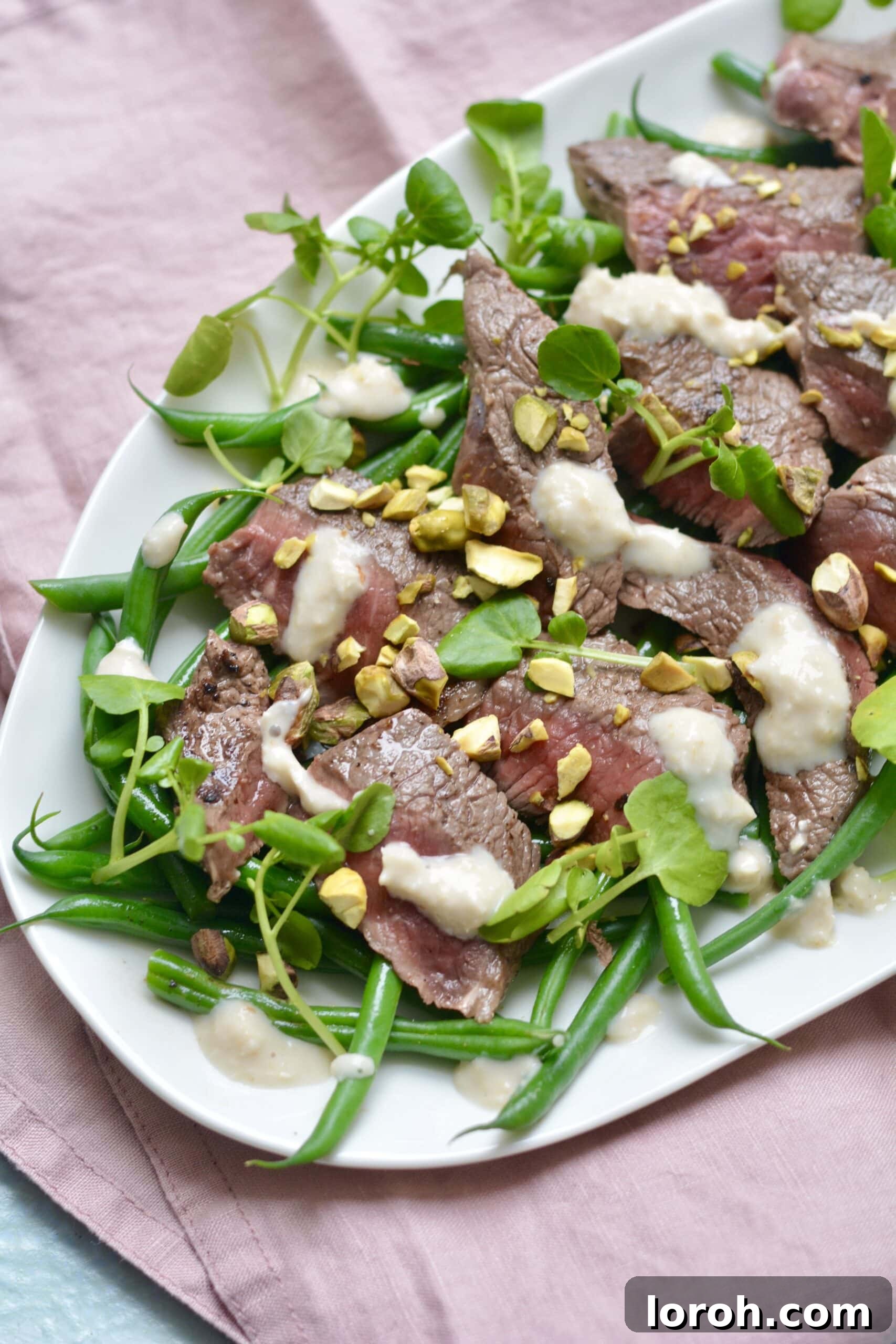 Perfectly seared steak with green beans and a drizzle of sauce on a plate