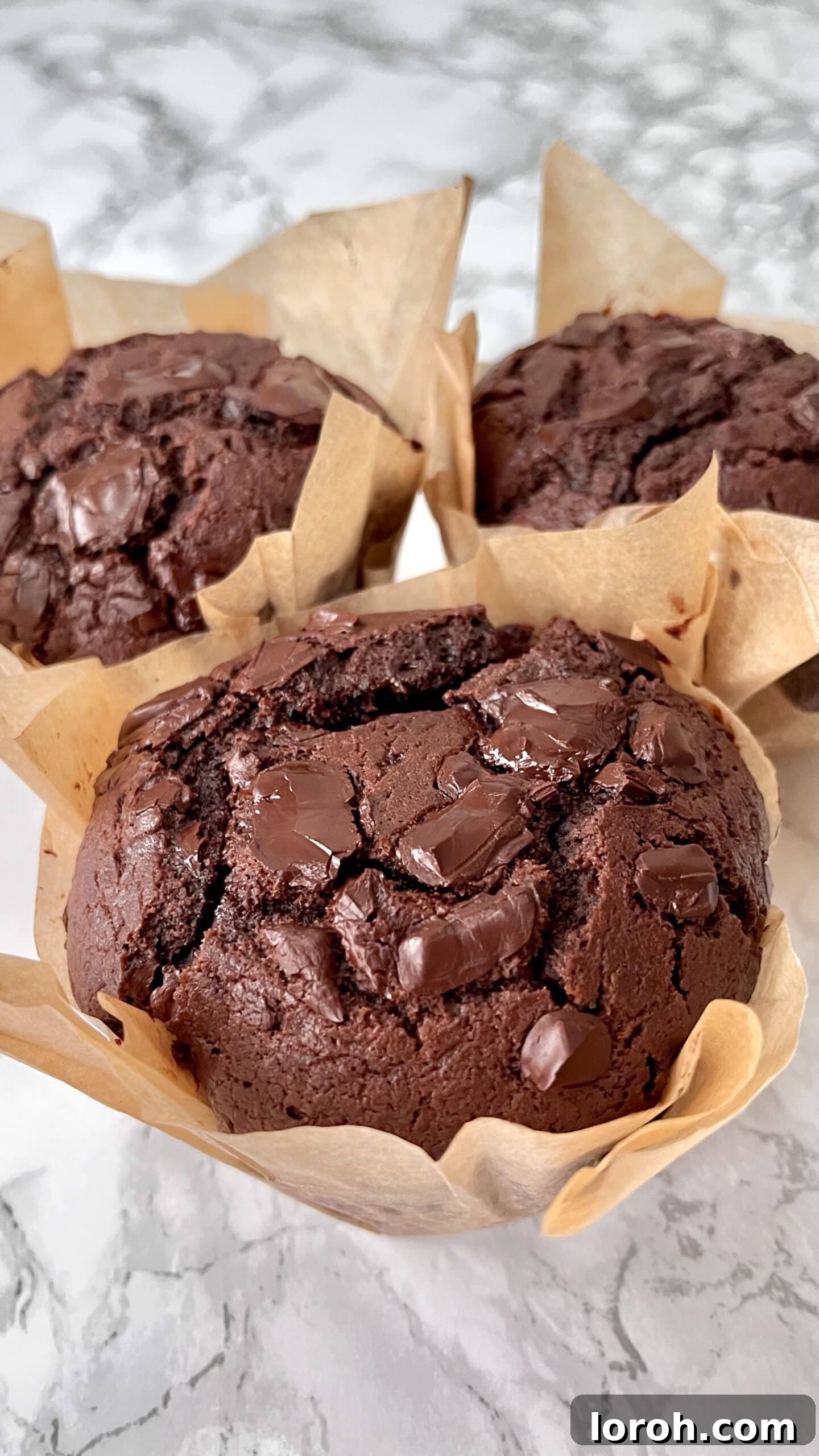Image of three perfectly baked chocolate chunk muffins in greaseproof liners, showcasing their golden-brown tops and rich chocolatey interior.