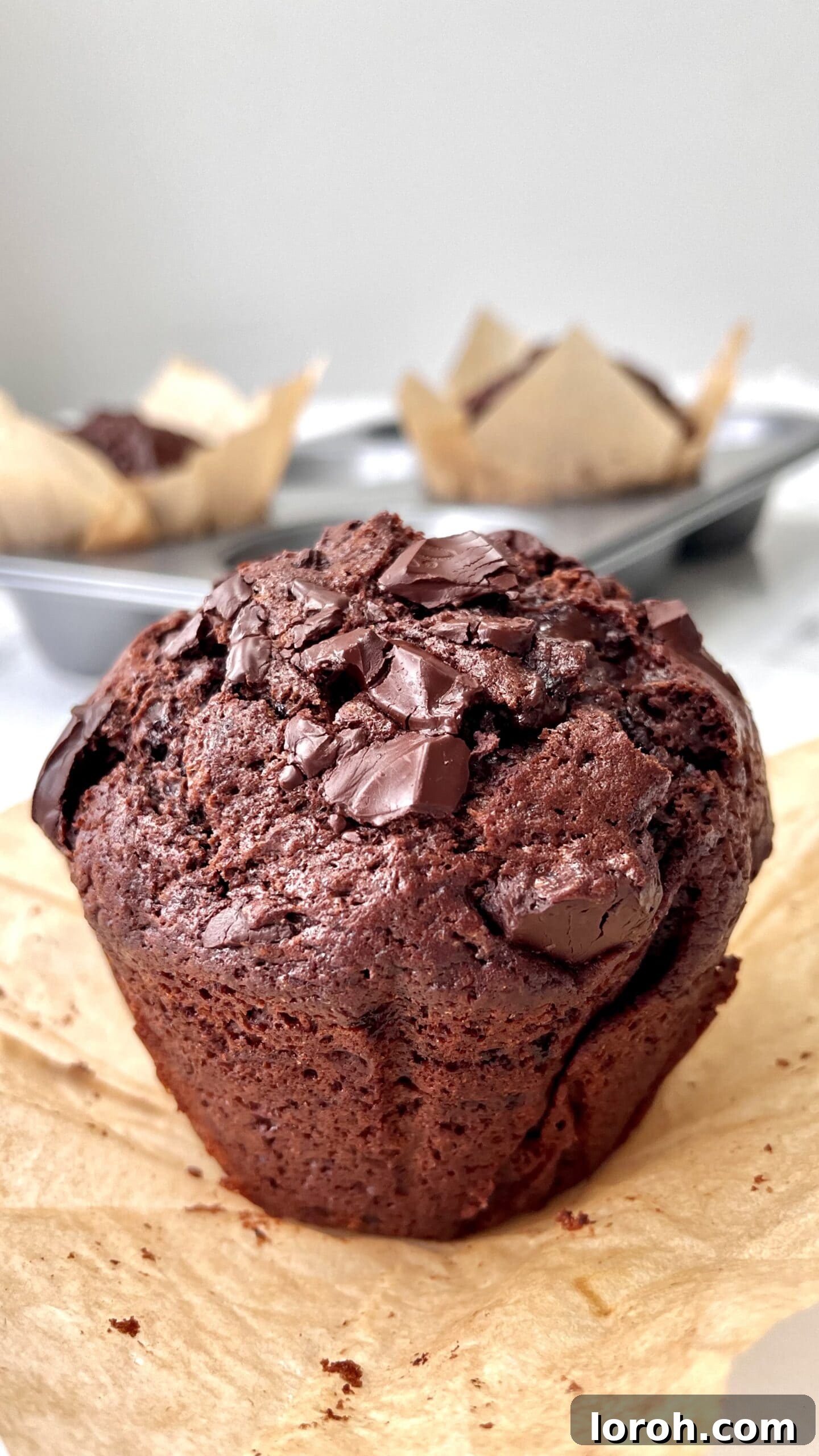 A single, perfectly baked chocolate chunk muffin presented on greaseproof paper, highlighting its inviting texture and visible chocolate chunks.