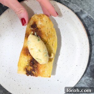 Woman with painted nails picking up a piece of toast with a piece of roasted garlic brown butter on the top.