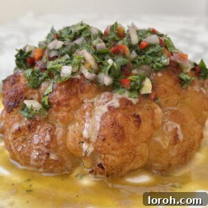 Close up of a whole roasted cauliflower with tahini sauce and chimichurri spooned over the top.