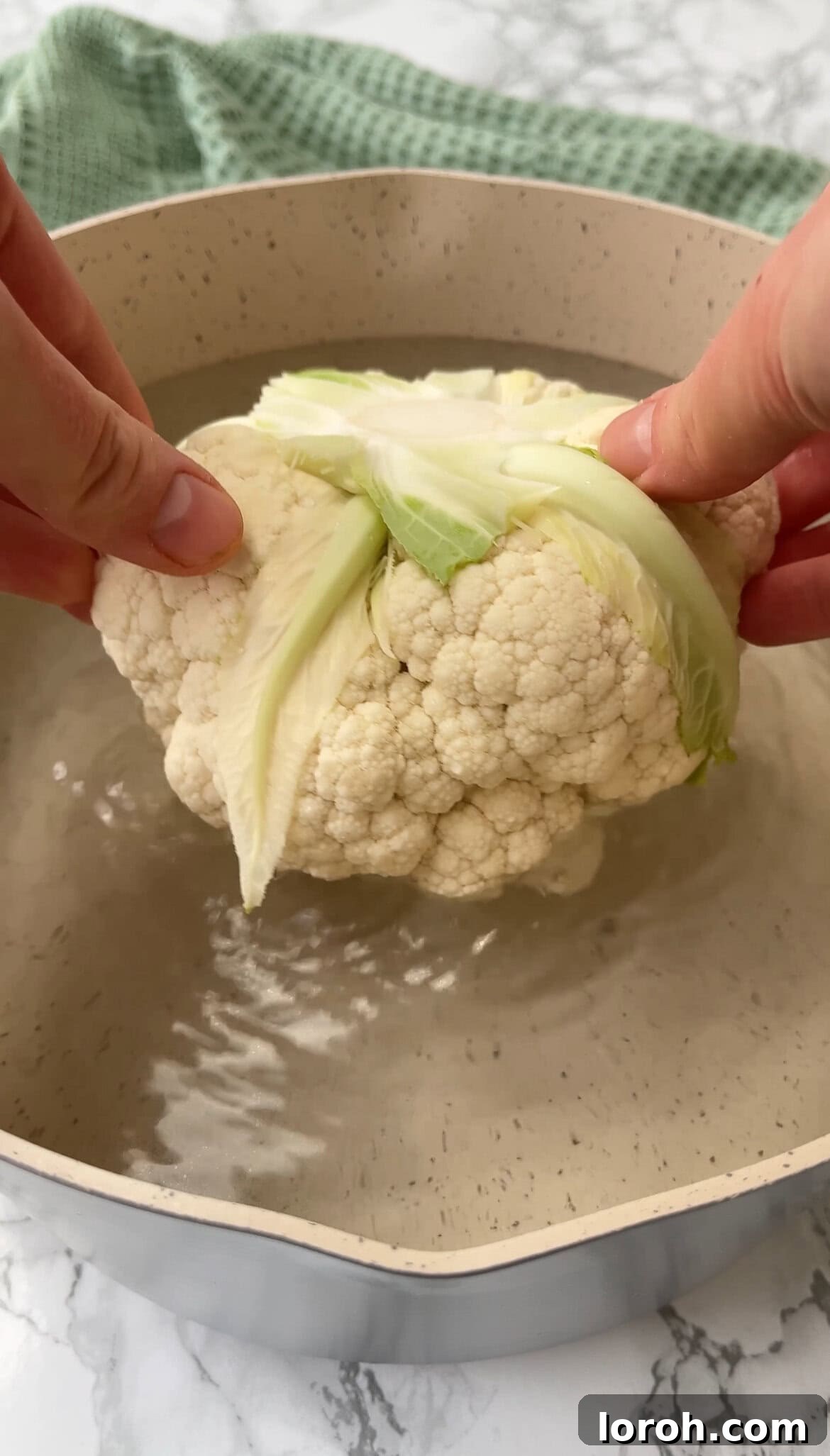 The Ultimate Whole Roasted Cauliflower with Tahini and Chimichurri 4 Large pot of water boiling with a whole cauliflower submerged, beginning the parboiling process.