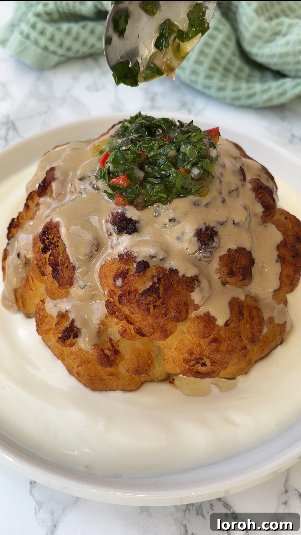 The Ultimate Whole Roasted Cauliflower with Tahini and Chimichurri 7 Roasted cauliflower topped with tahini and a vibrant green chimichurri sauce, showcasing the final presentation.