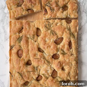 Golden focaccia bread topped with roasted garlic cloves and fresh rosemary sprigs, drizzled with olive oil.