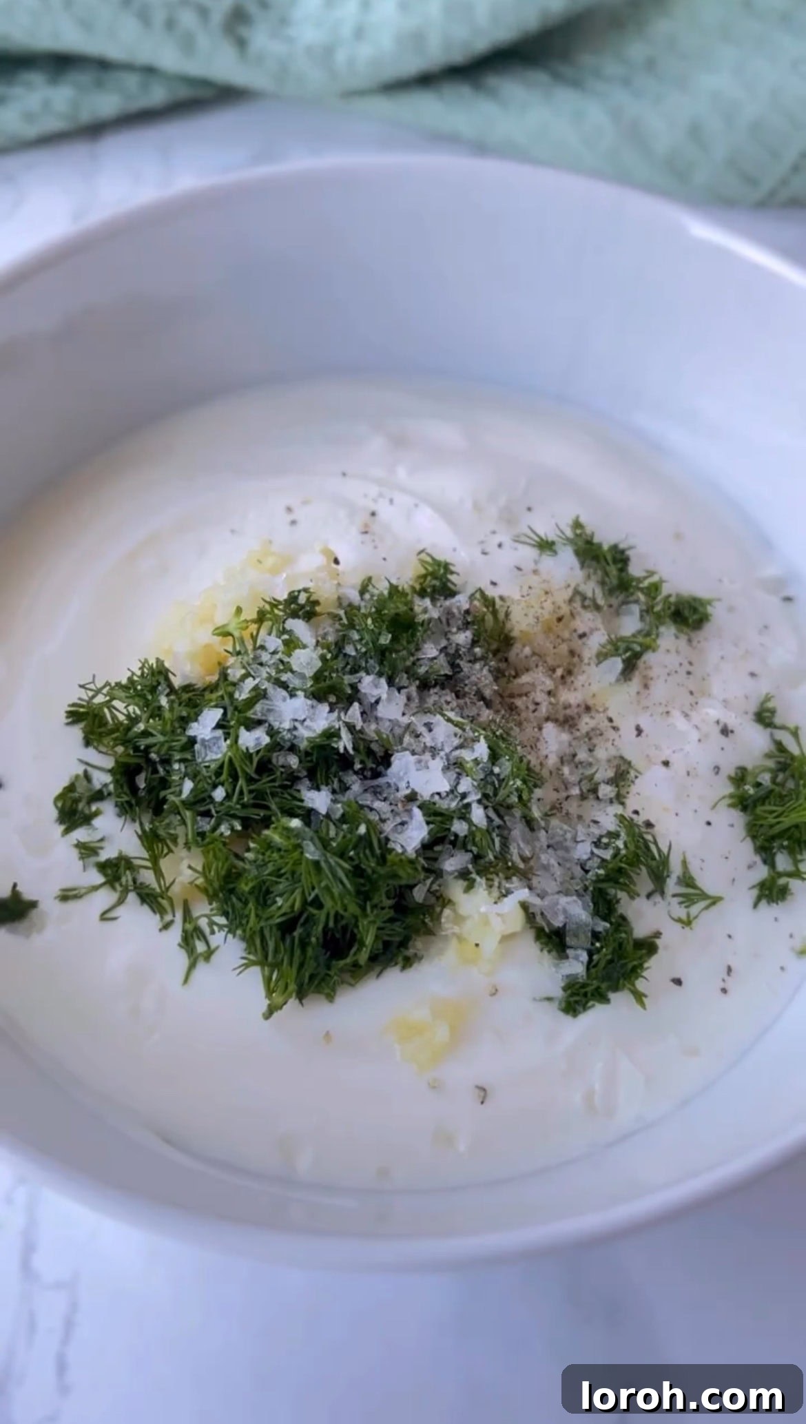 Mixing Greek yogurt, crushed garlic, and chopped dill for the creamy Çılbır base