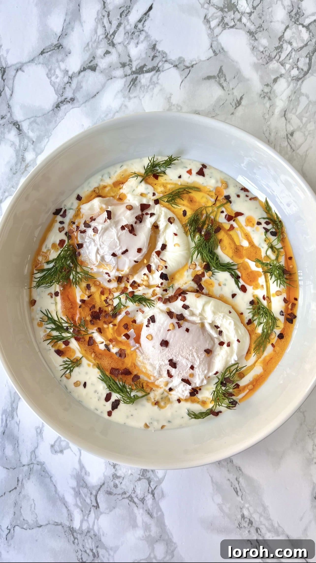 A vibrant bowl of Turkish eggs ready to be enjoyed, garnished with fresh herbs and a slice of bread