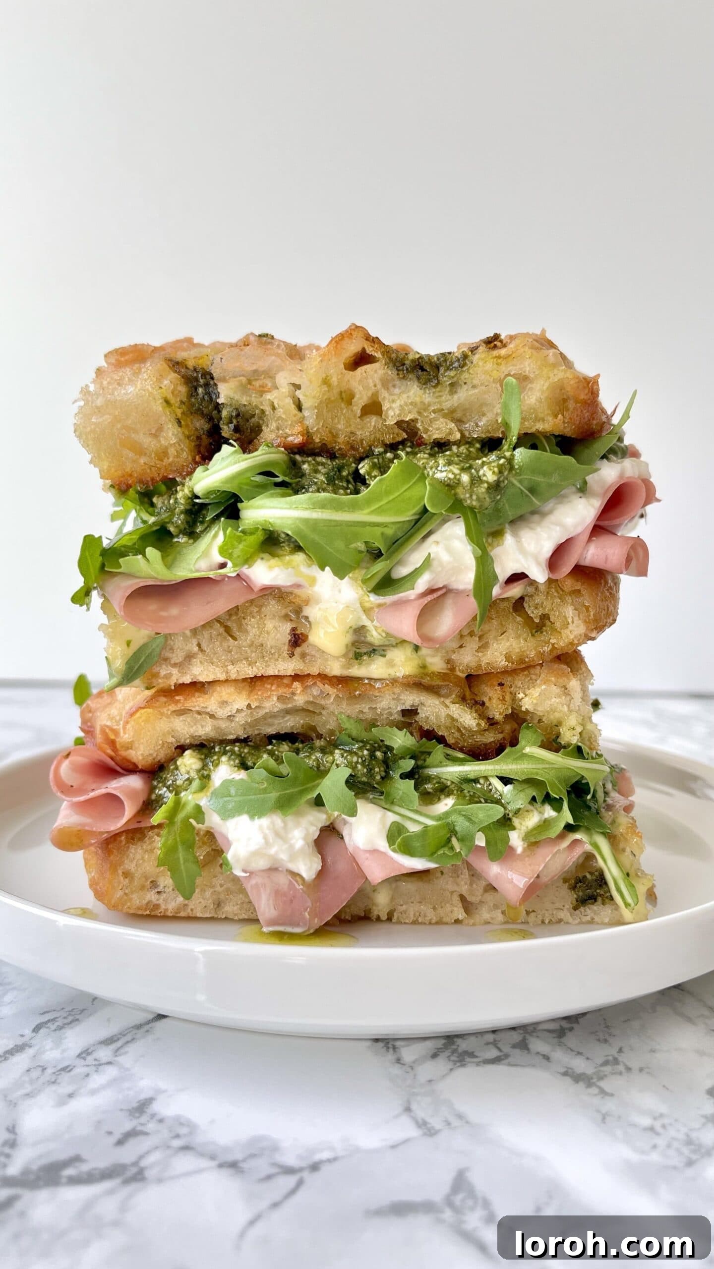 mortadella burrata sandwich with rocket, pesto, stacked on a plate