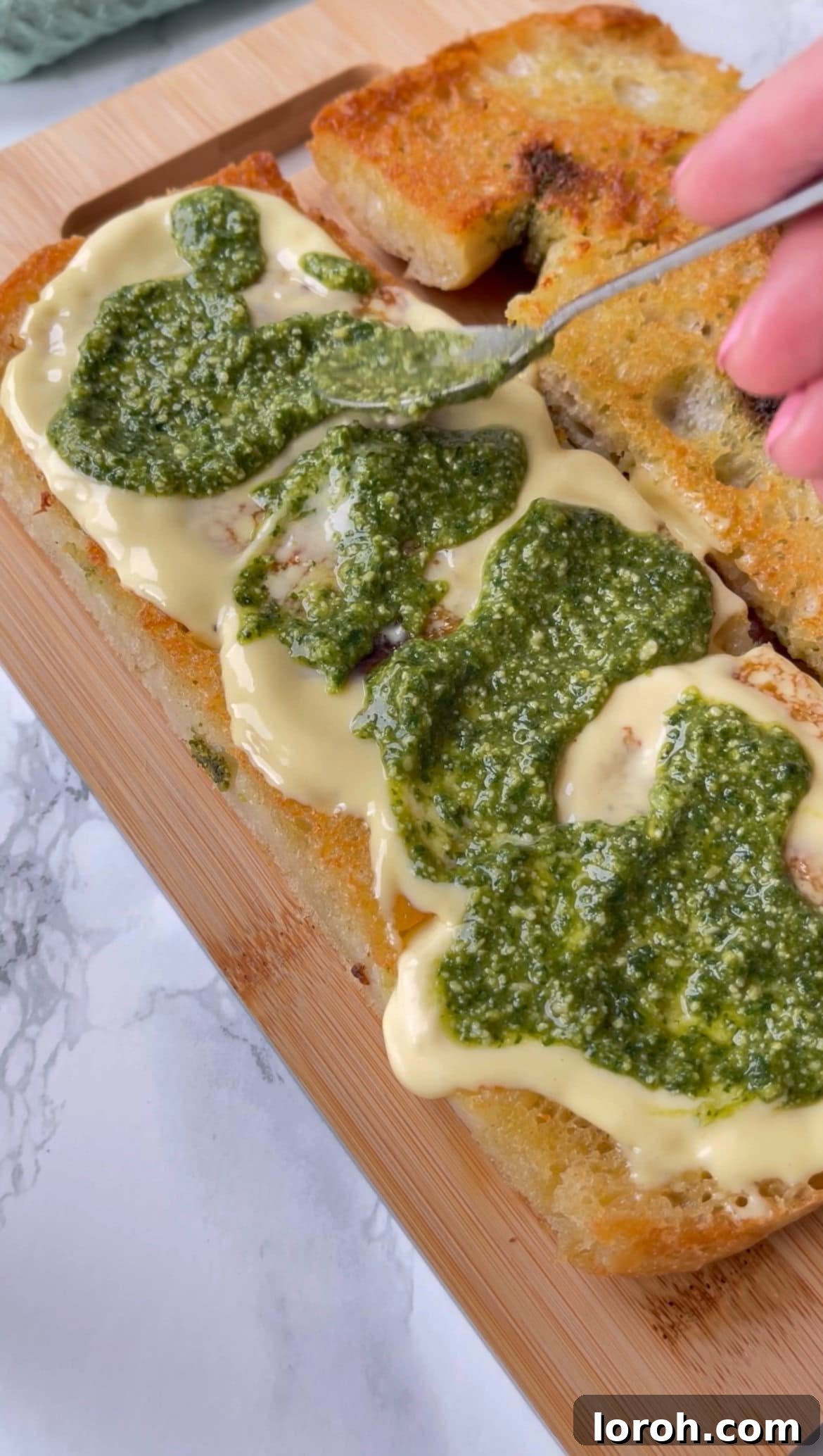 spreading pesto and aioli onto focaccia for mortadella burrata sandwich