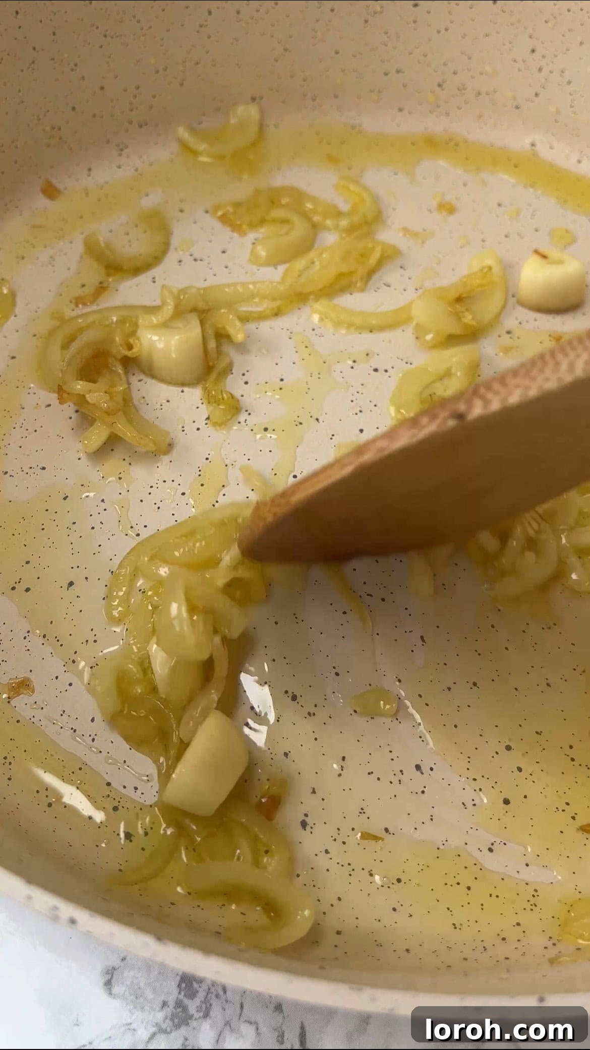 Sliced onion and garlic gently sautéing in shimmering olive oil in a large, wide pan.
