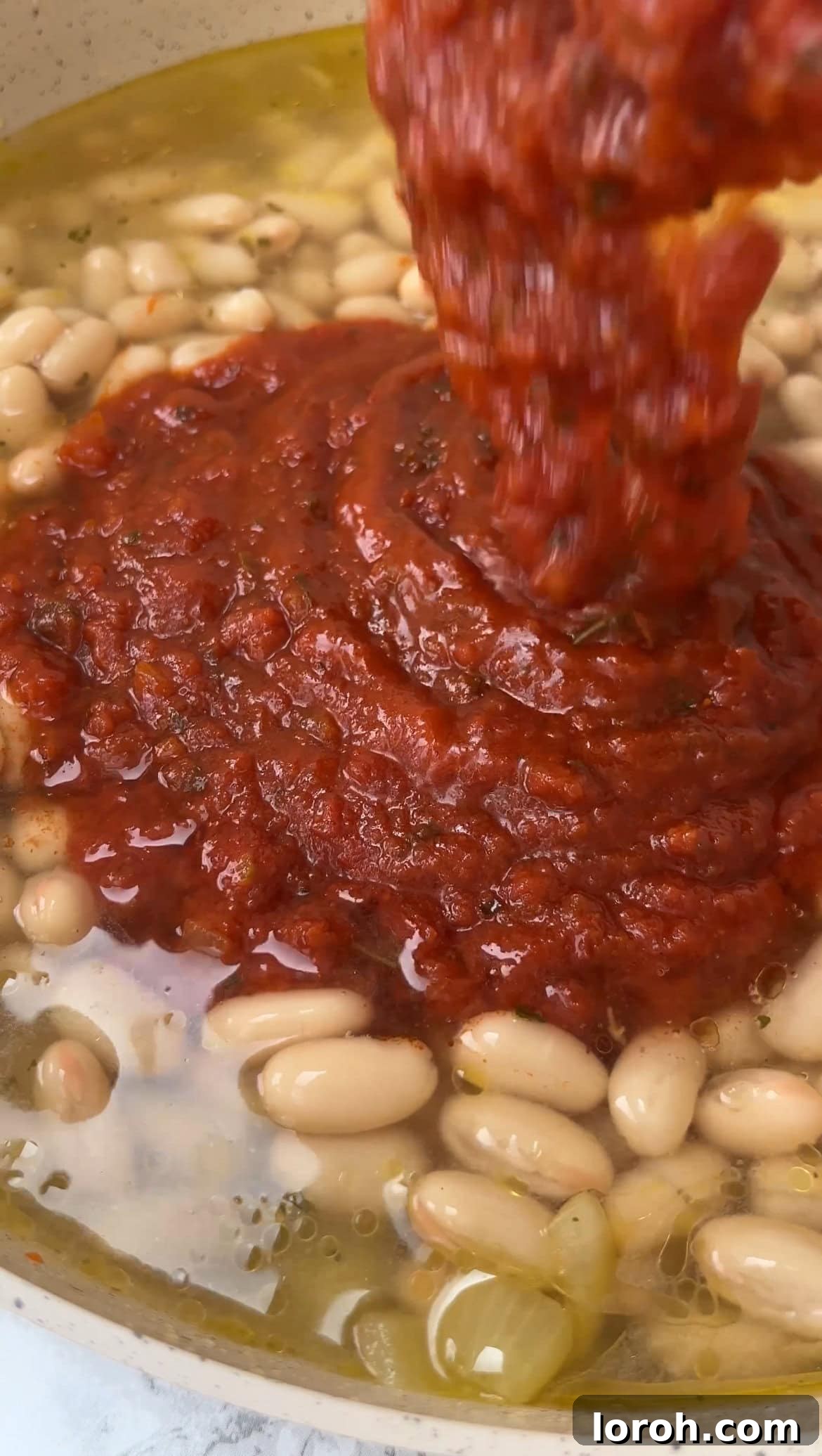 Cannellini beans, chicken stock, and marinara sauce being added to the fragrant sautéed onion and garlic in a pan, ready for simmering.