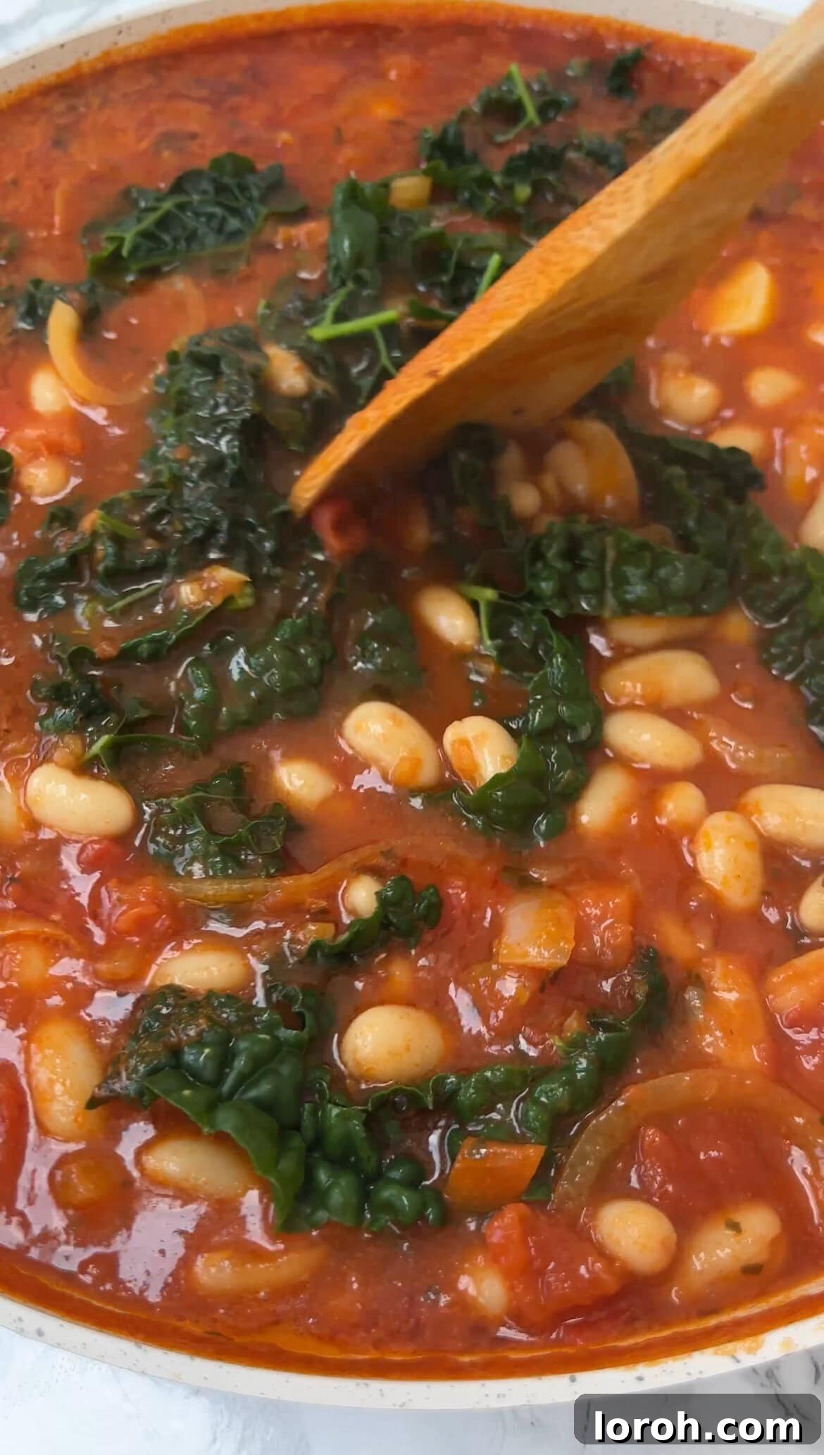 Tender, strained cavolo nero being stirred into the simmering bean mixture in the pan, integrating the greens into the rich sauce.