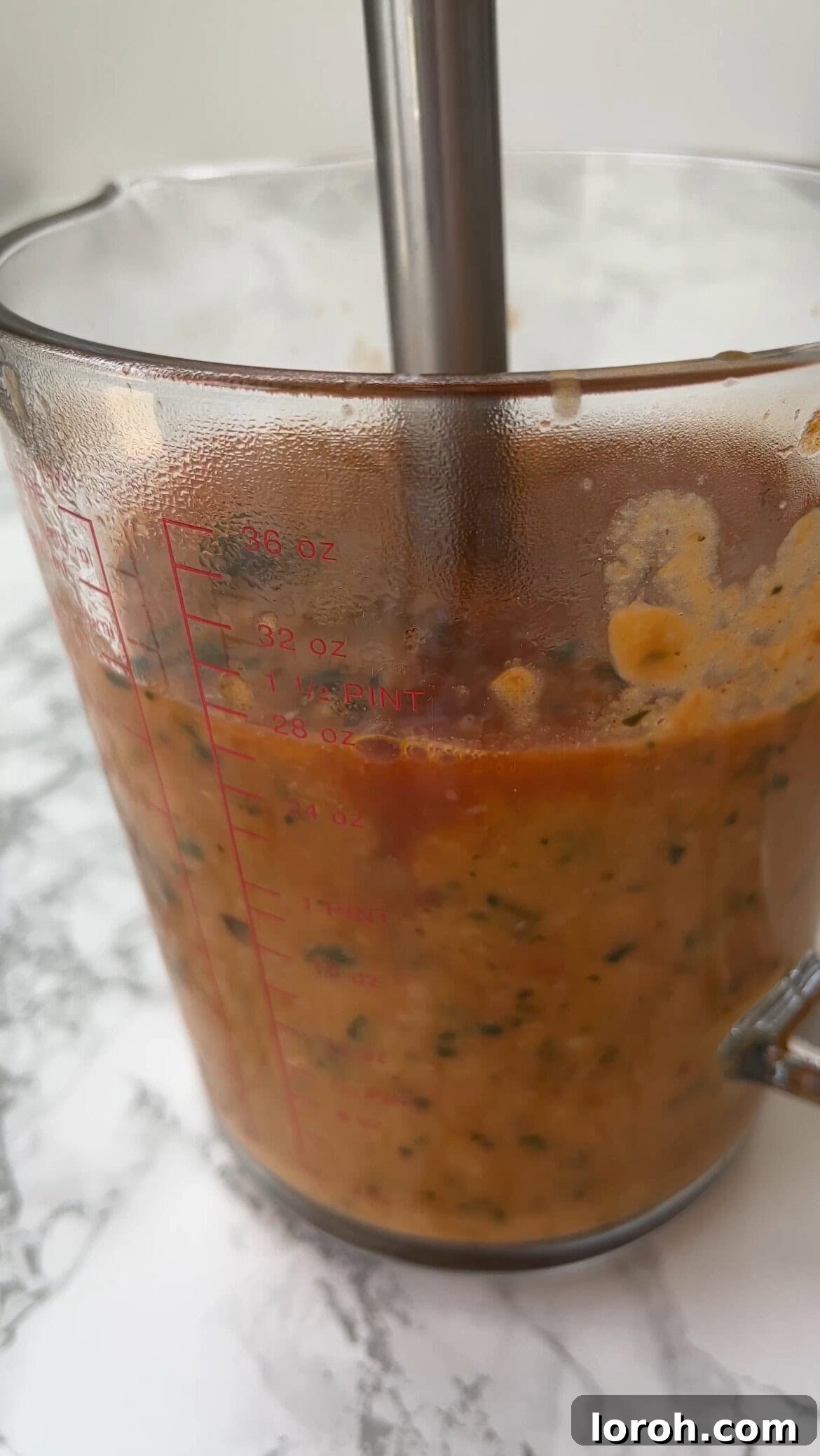Half of the cooked bean and tomato mixture being carefully scooped from the pan into a high-speed blender.