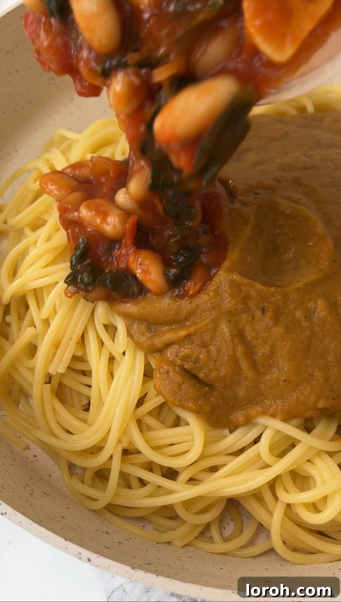 Cooked spaghetti being gently tossed with both the chunky and pureed bean mixtures in a large bowl, ready for final seasoning and serving.