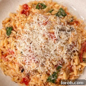 Bowl of tomato orzo with basil topped with grated parmesan.