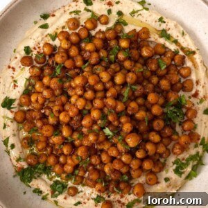 A beautifully garnished bowl of homemade hummus with a drizzle of olive oil, paprika, and fresh parsley, served with pita bread.
