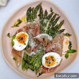 Asparagus on a pink plate topped with Parma ham, Parmesan, and a soft-boiled egg, drizzled with basil oil.