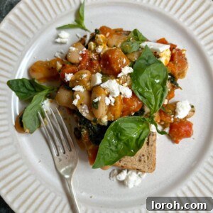 A vibrant plate of Tomato and Butterbeans on Toast, topped with crumbled feta and fresh basil leaves
