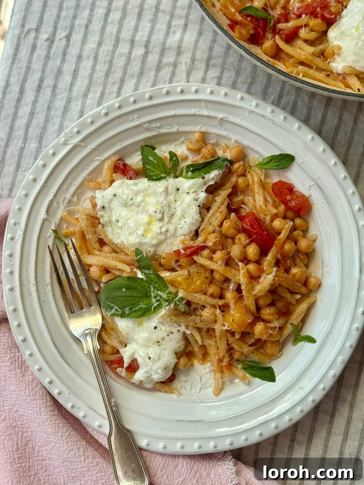 A plate of trofie pasta with bursting cherry tomatoes, chickpeas, and fresh mozzarella, garnished with basil.