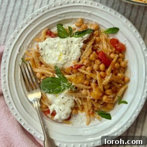A beautifully plated dish of trofie pasta with bursting tomatoes, chickpeas, mozzarella, and fresh basil.