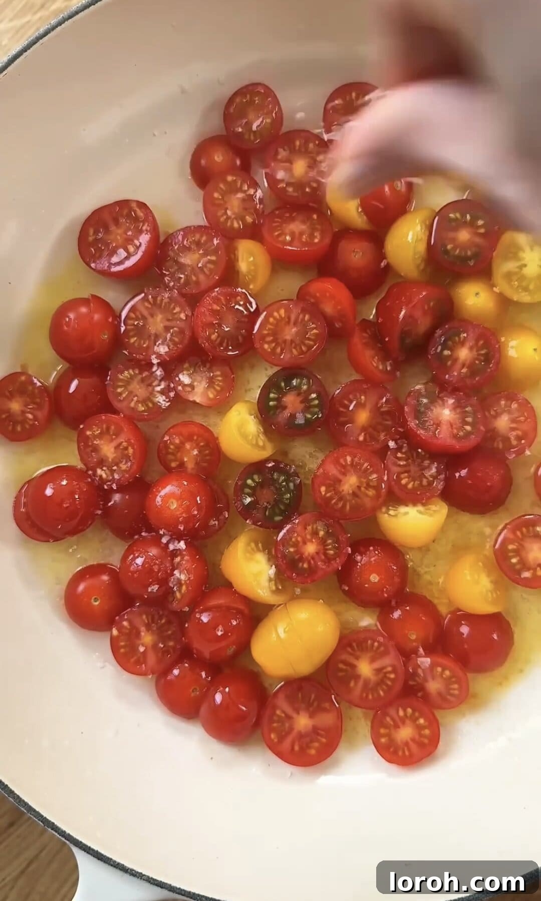 Halved cherry tomatoes being seasoned with salt in a hot pan with olive oil.