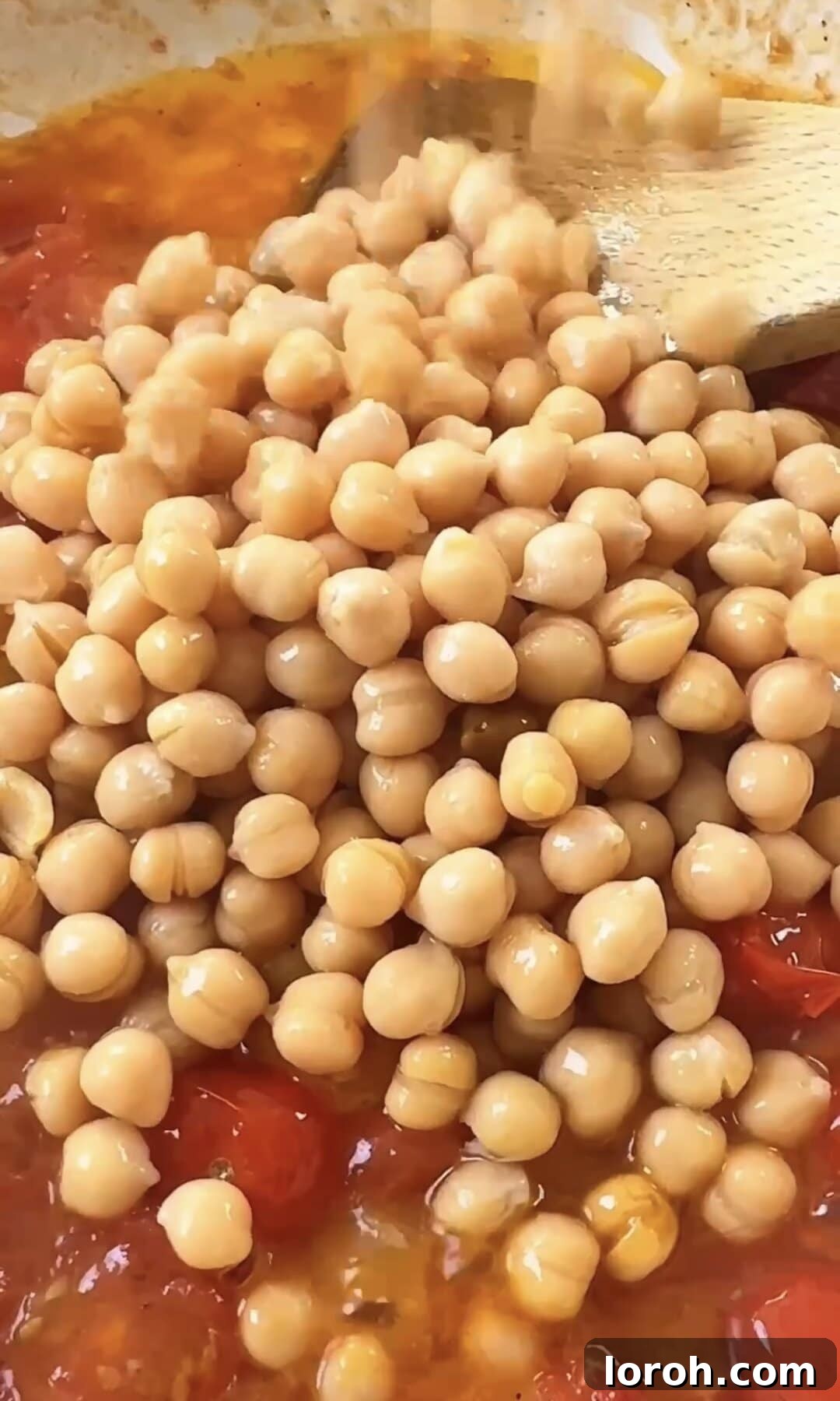 Chickpeas and their liquid being added to the pan of bursting tomatoes.