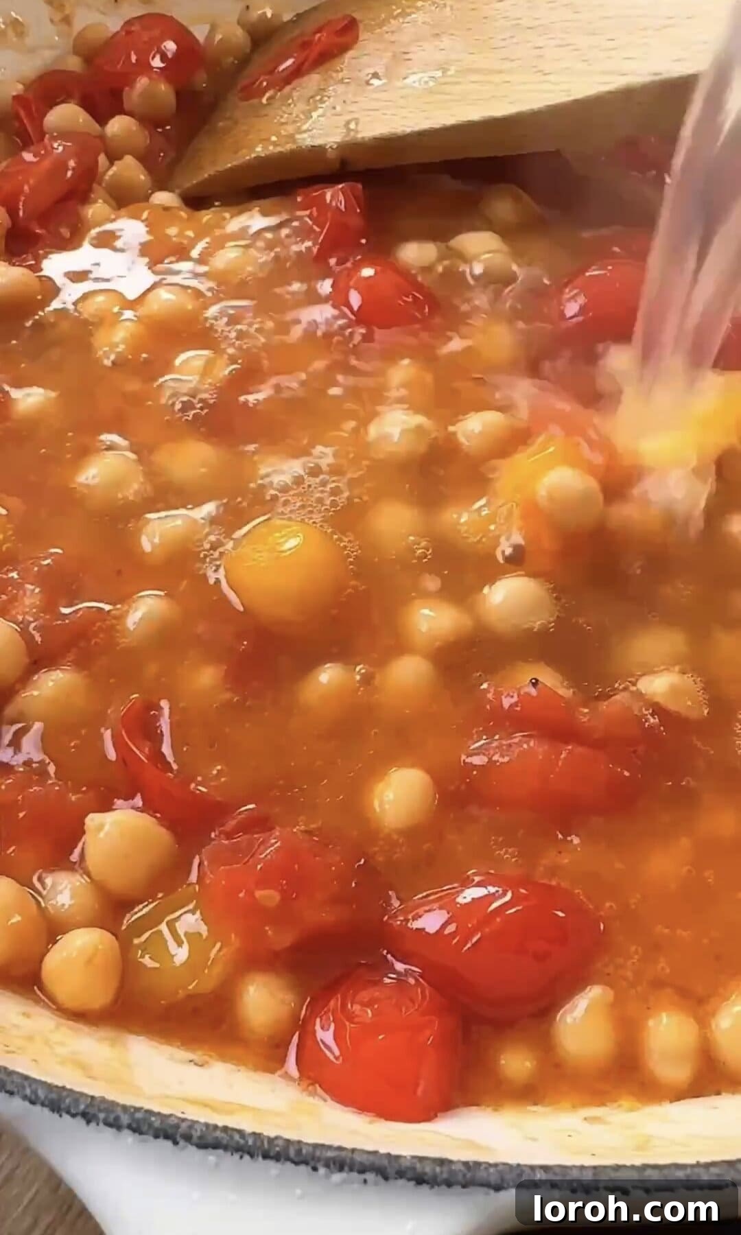 Adding pasta water to the simmering tomato and chickpea sauce in a pan.