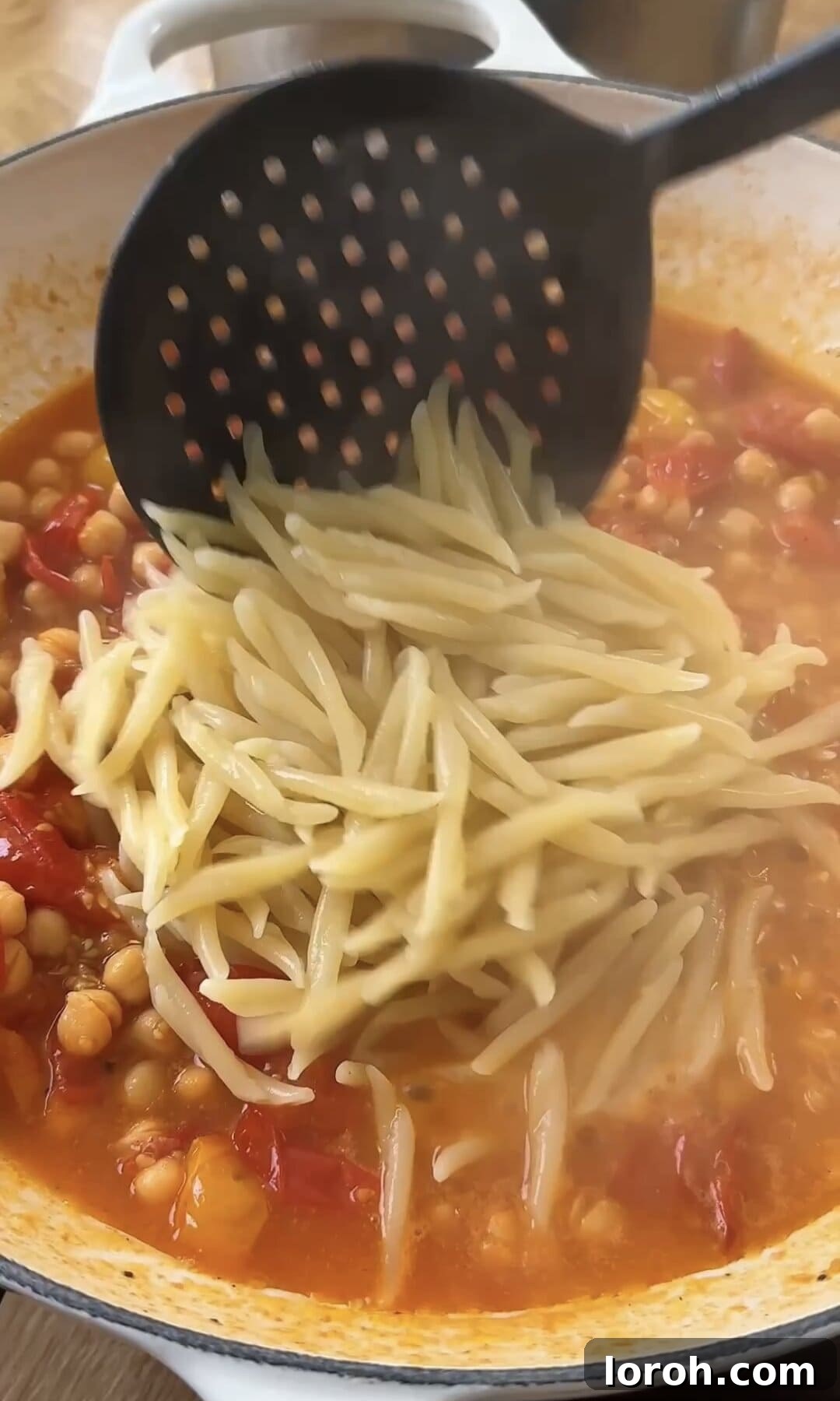 Cooked trofie pasta being added directly into the pan with the tomato and chickpea sauce.