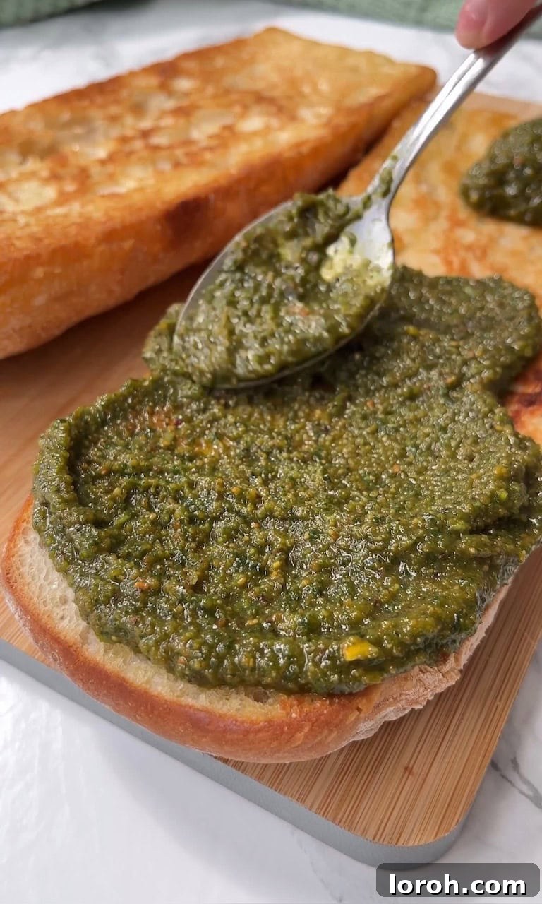 Burrata Caprese Prosciutto Sandwich Drizzled with Pistachio Pesto 8 Spreading vibrant green pistachio pesto evenly onto a halved ciabatta bread.