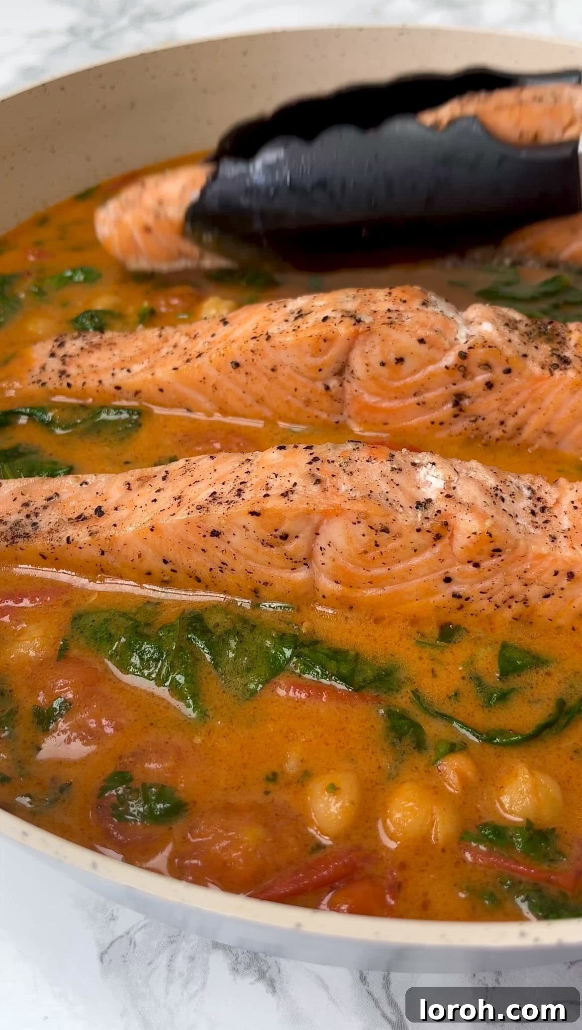Gently placing seared salmon fillets into the simmering Thai curry with spinach and coriander.