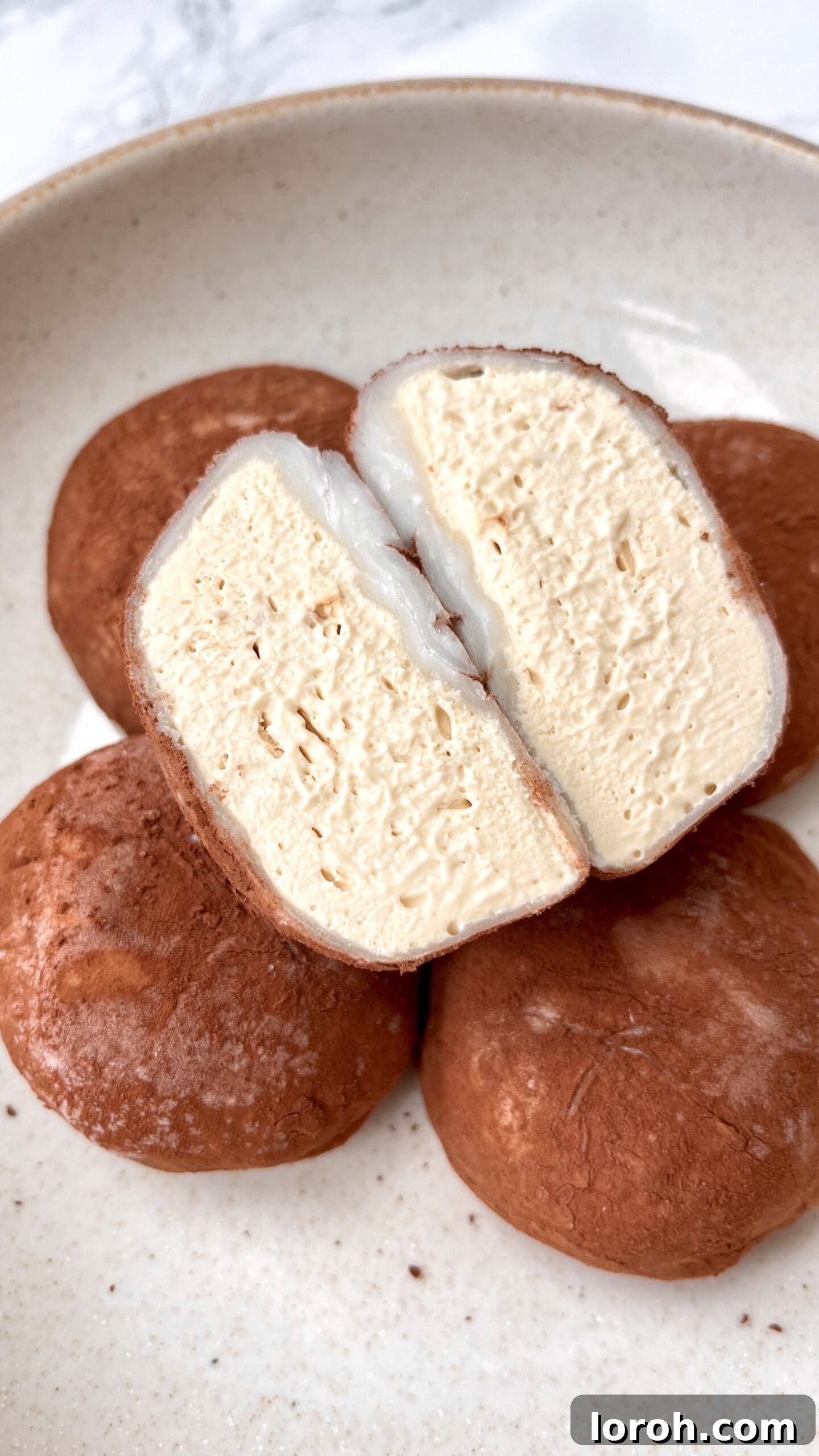 Cross-section of a Tiramisu Ice Cream Mochi Bite, revealing coffee and chocolate ice cream inside a white mochi shell.
