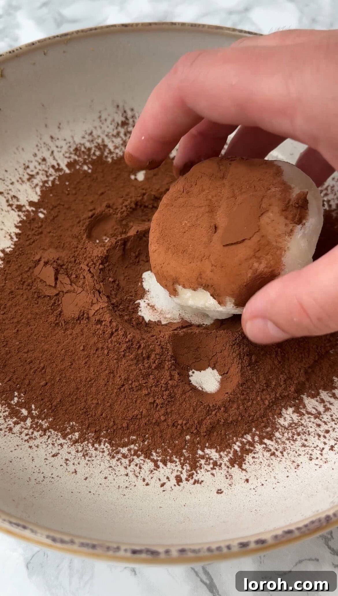 Rolling a finished mochi bite in cocoa powder for a tiramisu finish.
