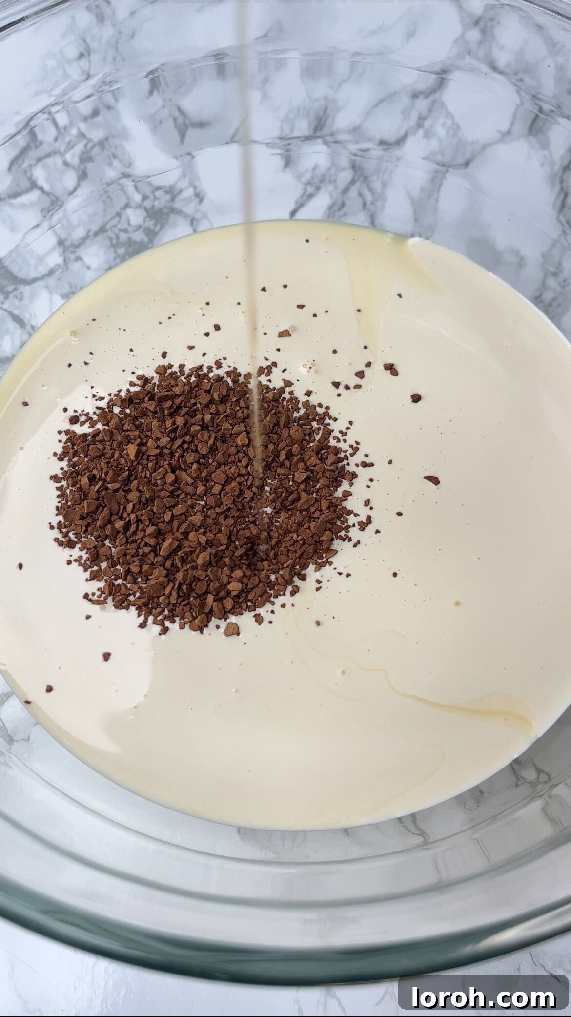 Adding instant coffee powder to a bowl of condensed milk, cream, and vanilla for ice cream.