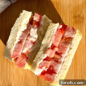 A beautifully prepared classic tomato sandwich, cut in half, showcasing vibrant red tomato slices and creamy mayonnaise.