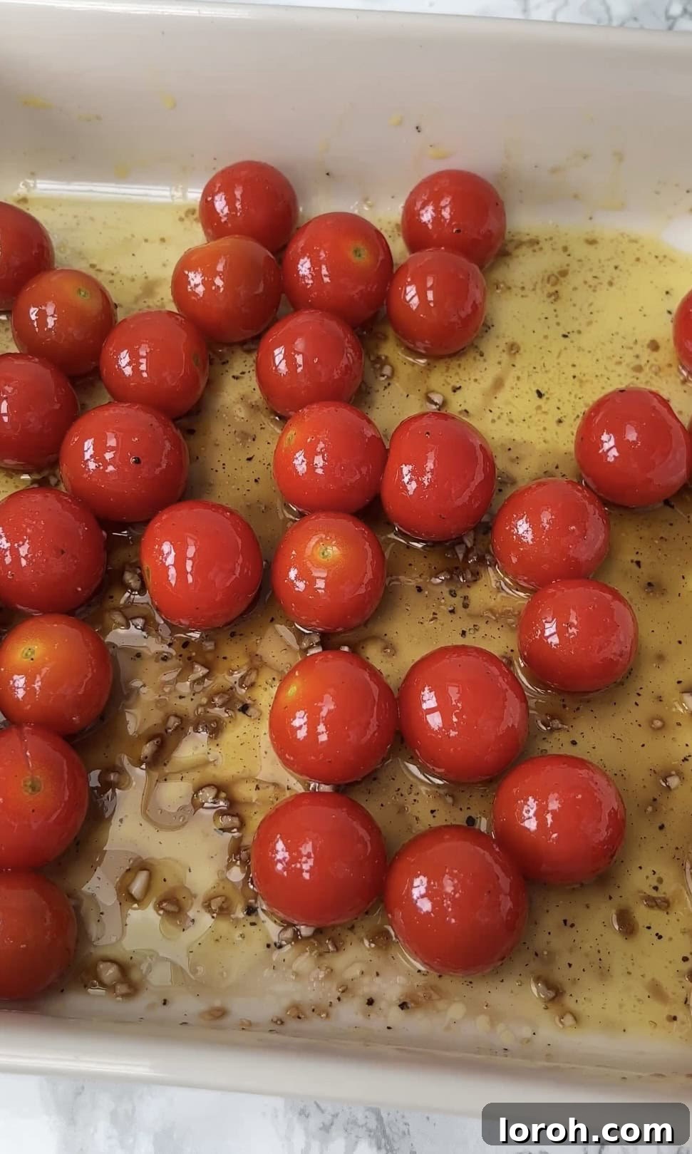 Close-up of cherry tomatoes, garlic, and balsamic vinegar drizzled with olive oil in a baking dish, ready for roasting.
