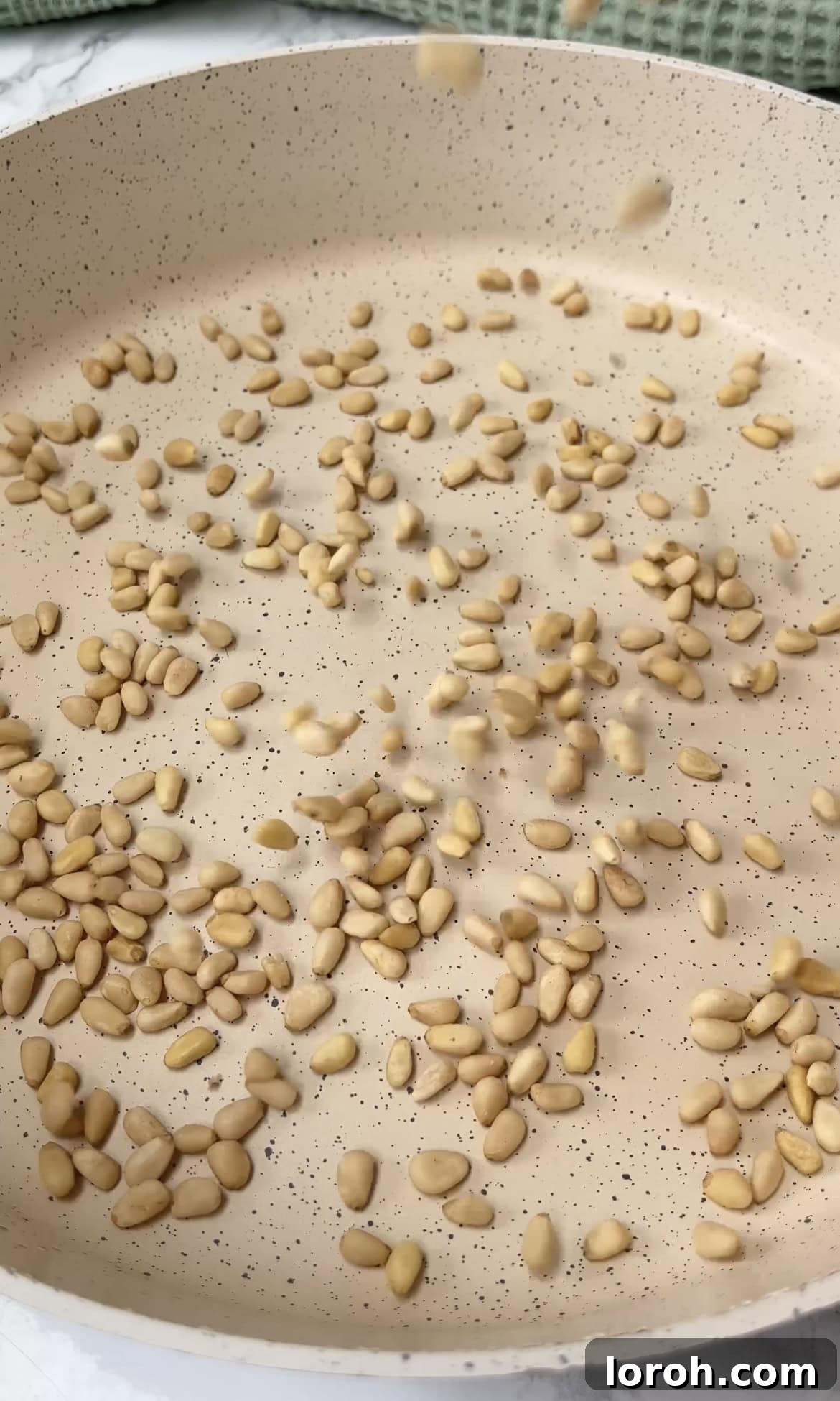 Pine nuts toasting in a dry frying pan over medium-high heat, turning a light golden brown.