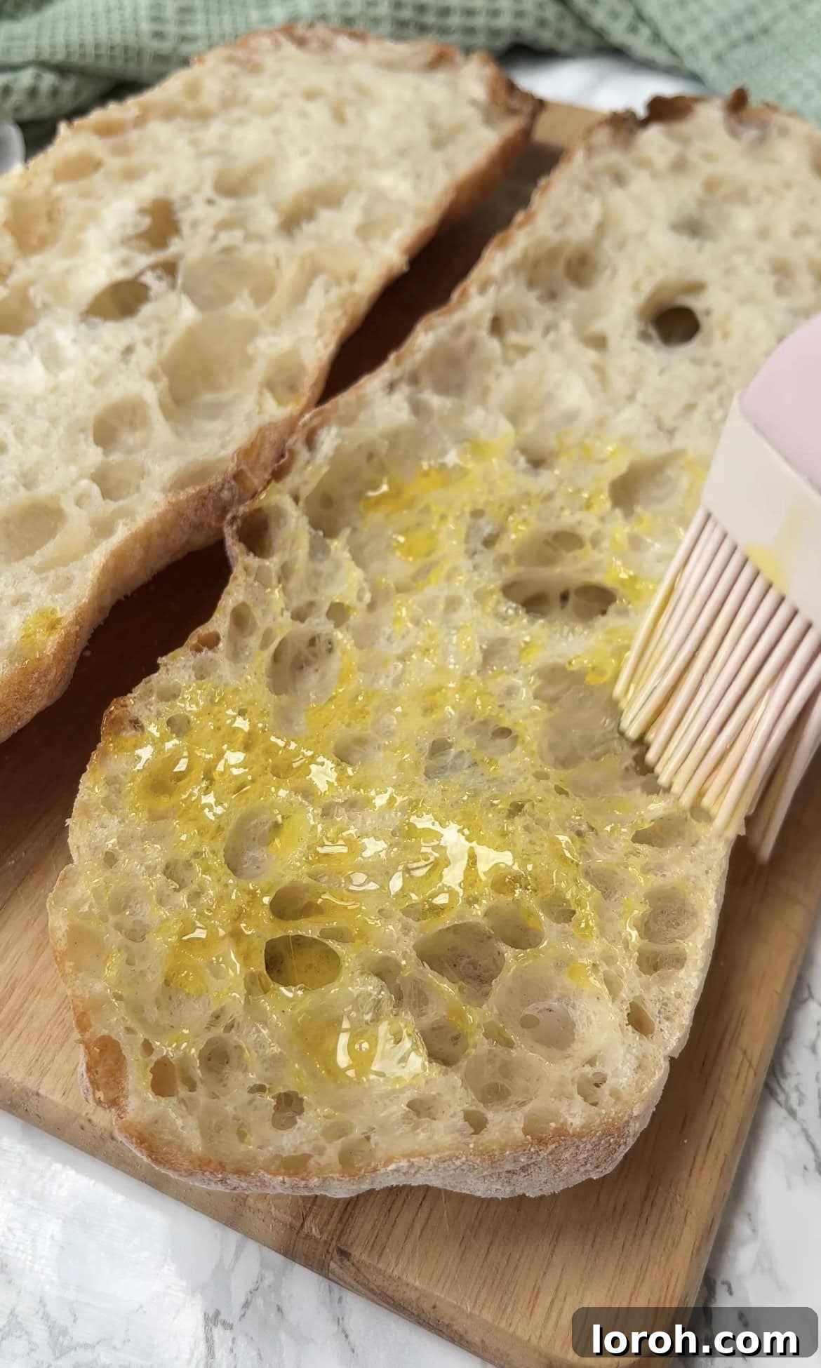 Slices of ciabatta bread being brushed with olive oil on both sides before toasting.