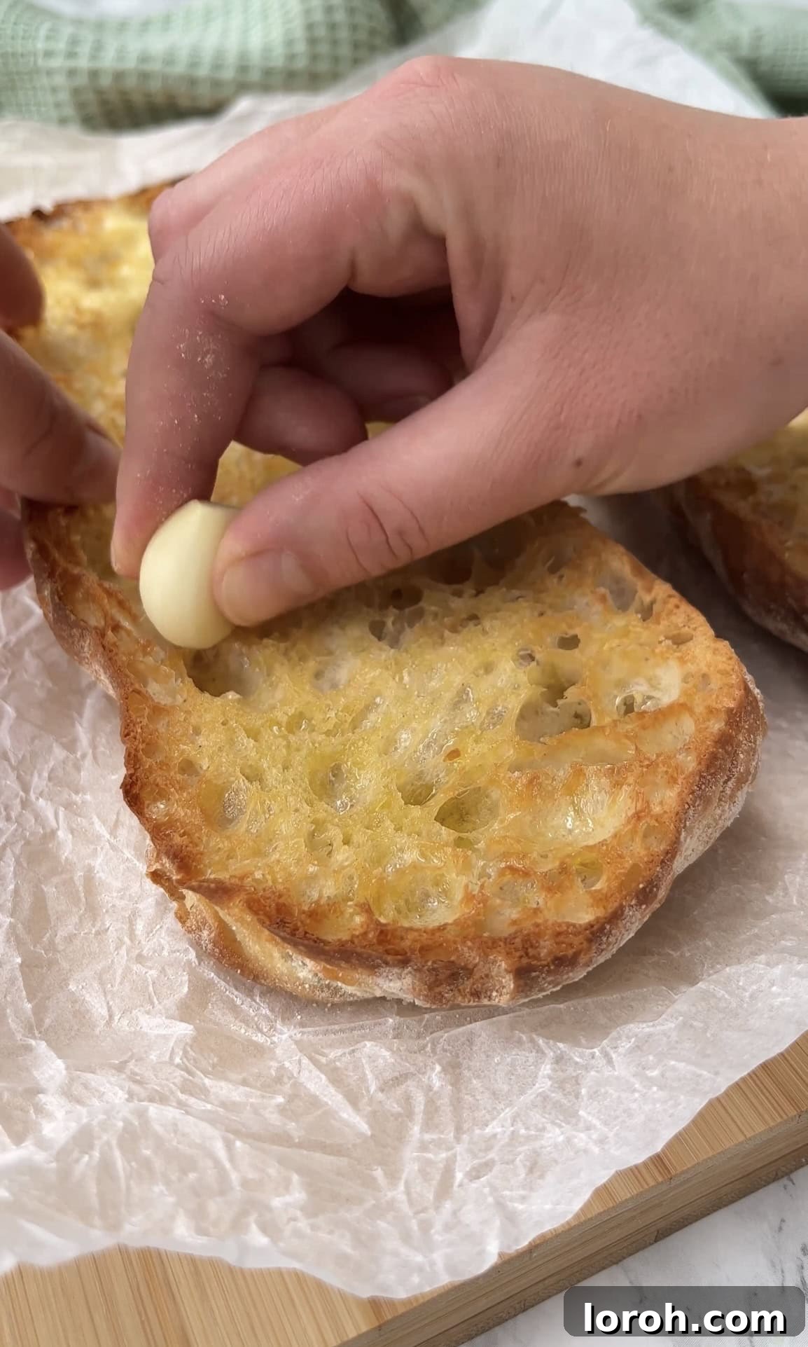 A toasted slice of ciabatta bread being vigorously rubbed with a raw garlic clove to infuse it with flavor.