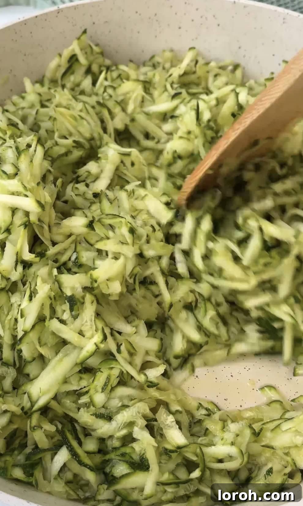 Grated courgettes sizzling gently in olive oil within a large frying pan.