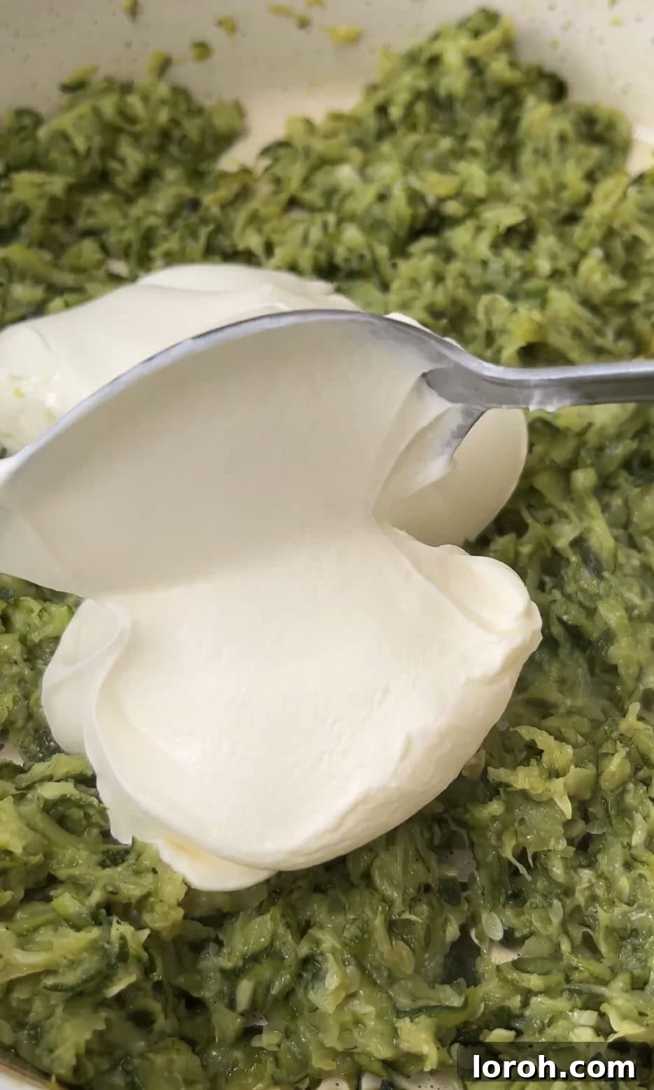 A generous dollop of crème fraîche being stirred into the sautéed courgettes and garlic.