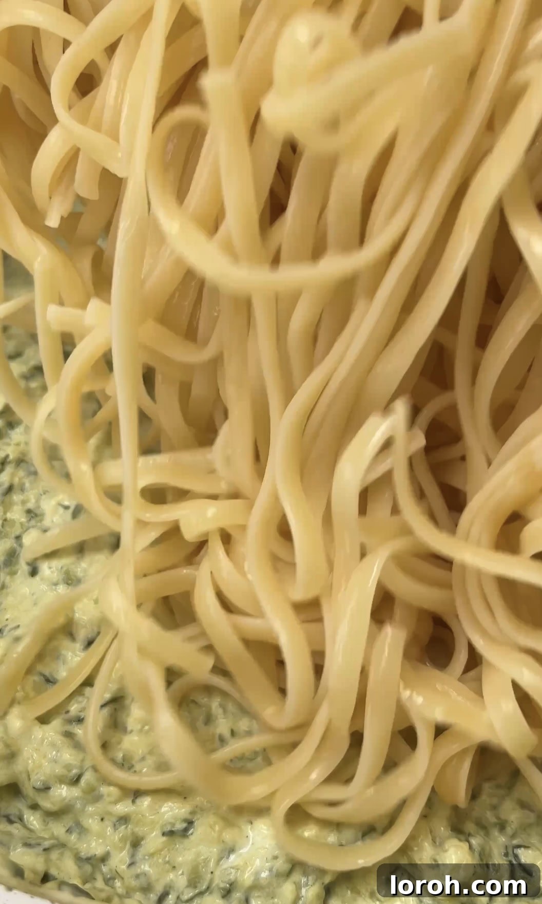 Al dente linguine being added directly into the creamy courgette sauce in the pan.
